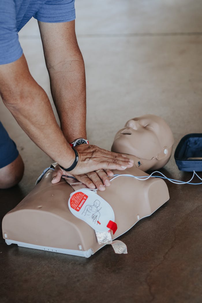 creative-01 Hands demonstrating CPR technique on a training mannequin with AED.